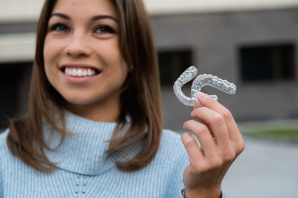Caucasian woman with white smile holding transparent removable retainer. Bite correction device